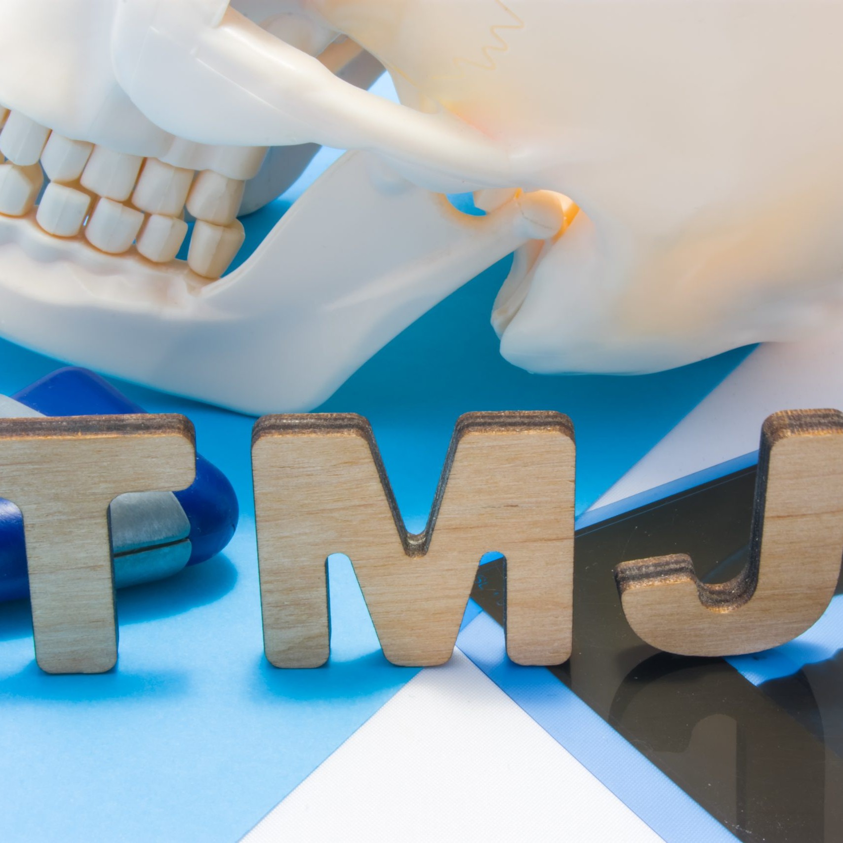 TMJ medical abbreviation of temporomandibular joint. TMJ letters surrounded by human skull with lower jaw, neurological hammer and radiographs. Concept of anatomy, pathology of temporomandibular joint